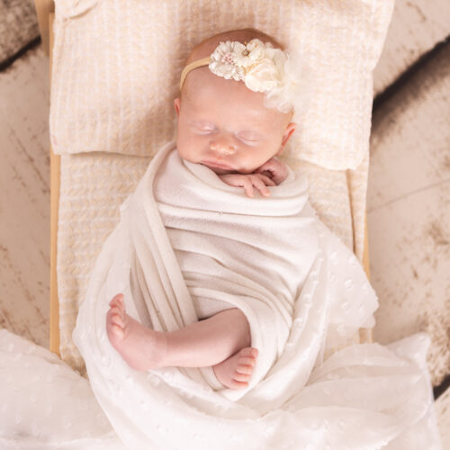 Petit bébé dort dans un lit en bois avec un headband fleuri, séance newborn à Caen