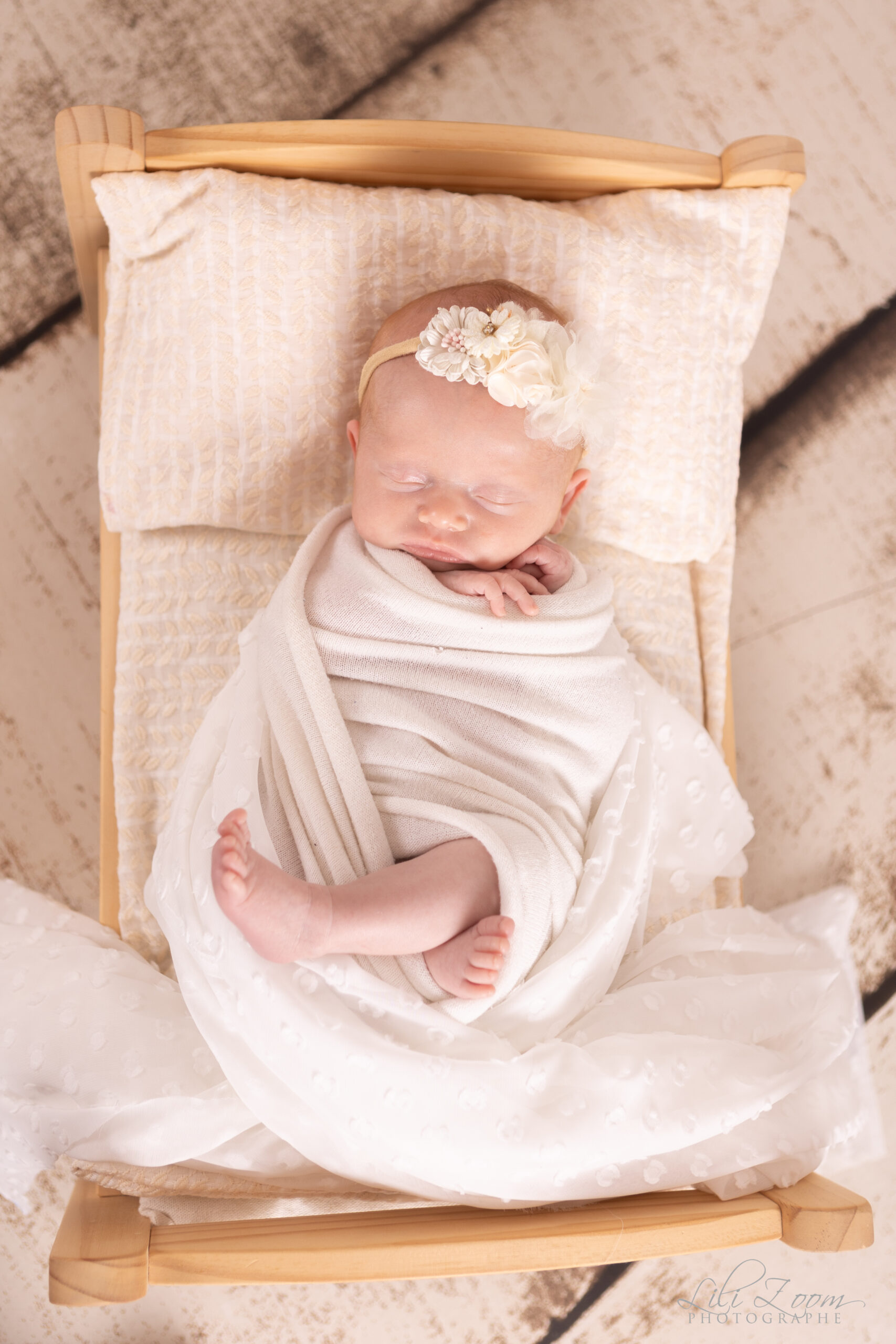 Petit bébé dort dans un lit en bois avec un headband fleuri, séance newborn à Caen