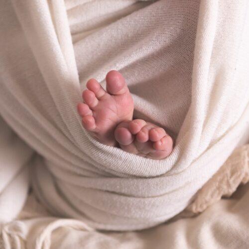 Photo macro de petit pieds d'un bébé emmailloté dans du lin, couleurs douces et naturelles esprit bohème, séance photo nouveau né à Caen