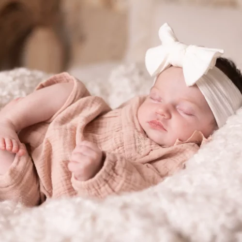 Nouveau-né endormi paisiblement dans un cocon de laine blanche avec un joli bandeau à nœud - Photographe Naissance à Giberville