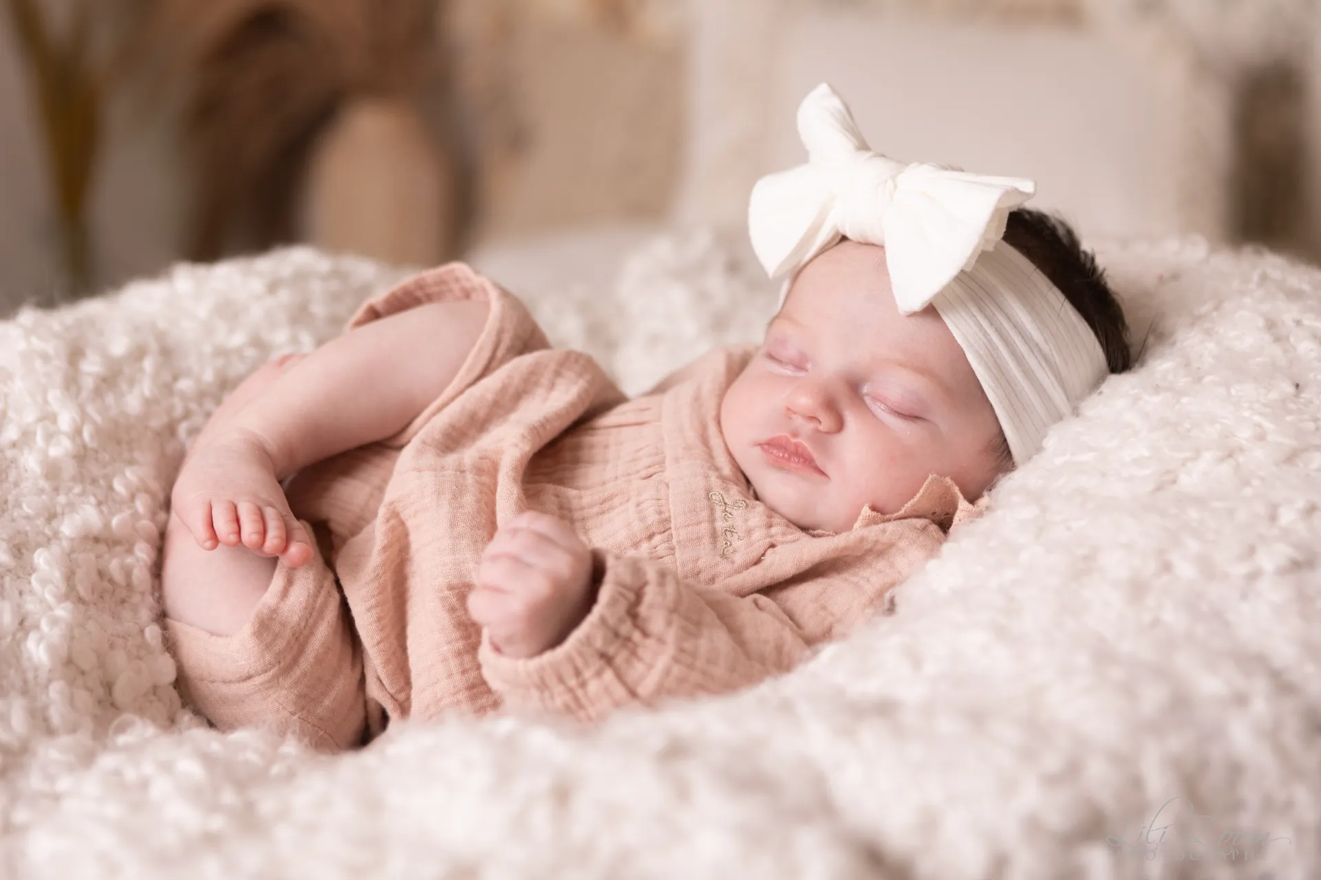 Nouveau-né endormi paisiblement dans un cocon de laine blanche avec un joli bandeau à nœud - Photographe Naissance à Giberville