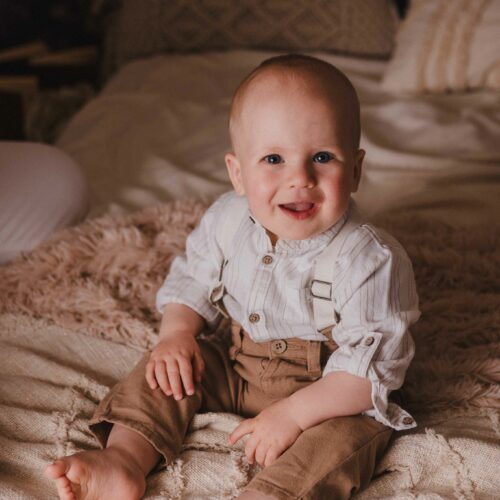 Un bébé avec des bretelles assis sur un lit dans un style bohème, séance photo à Caen