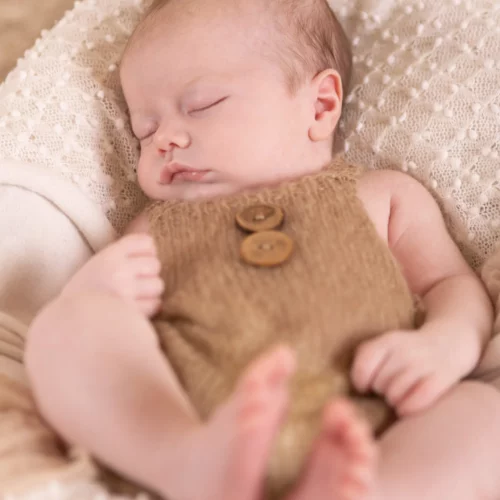Nouveau-né paisible endormi dans une petite tenue en laine marron sur un plaid texturé blanc - Photographe Naissance à Caen