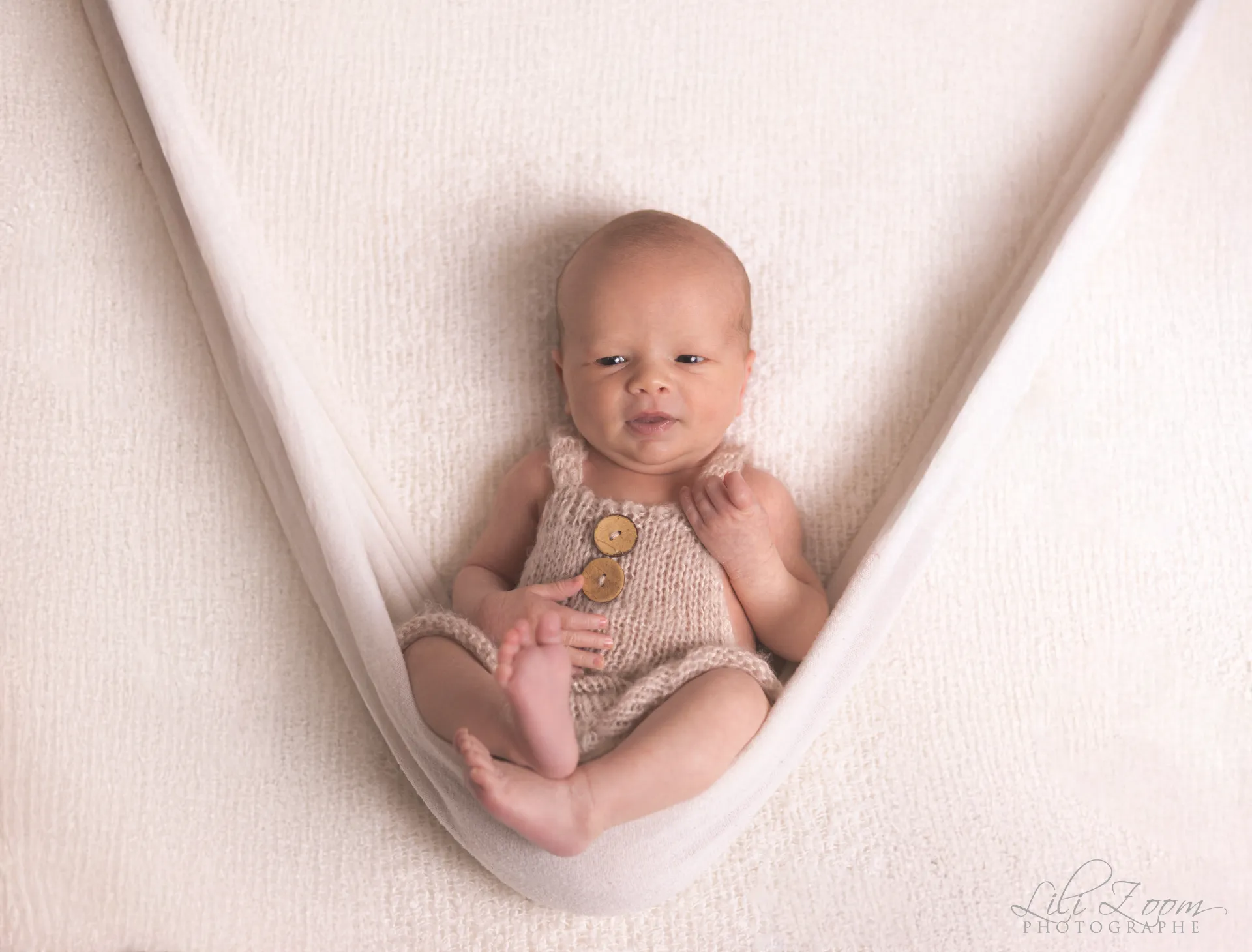 Nouveau-né éveillé installé confortablement dans un hamac en coton blanc - Photographe Naissance à Giberville