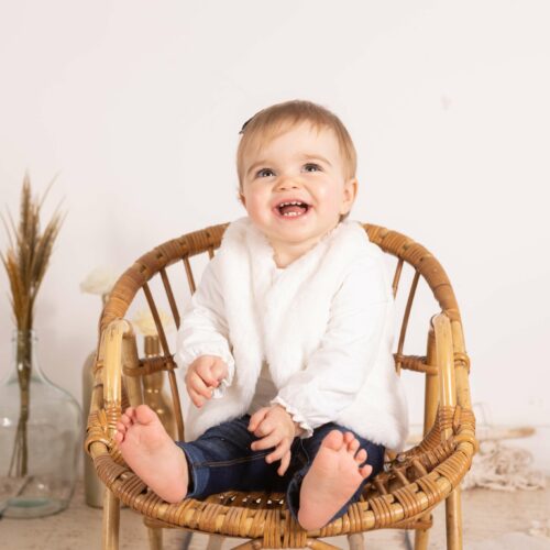 Bébé assis sur un fauteuil en rotin dans un studio photo au décor nature, séance photographie à Caen