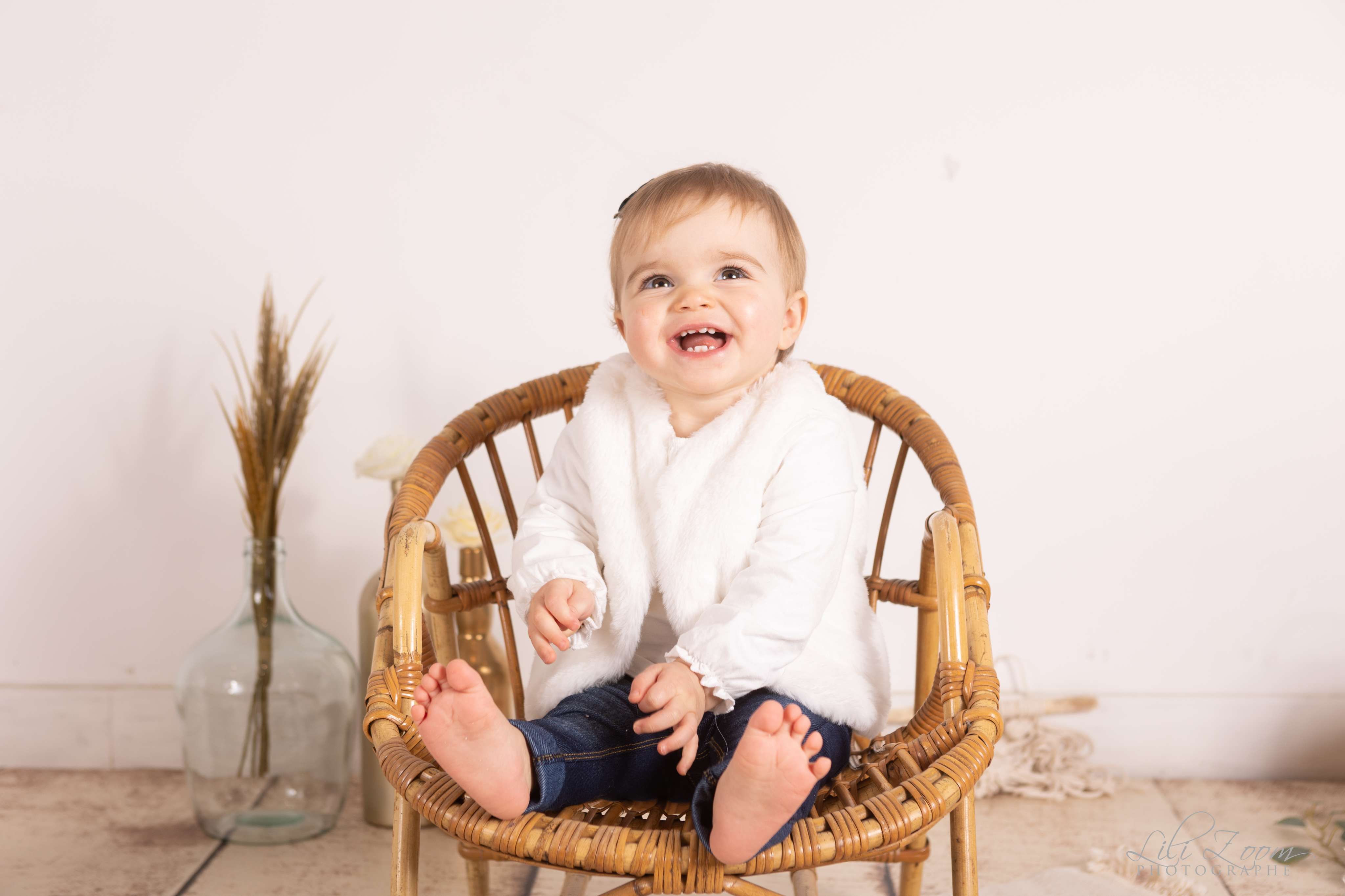 Bébé assis sur un fauteuil en rotin dans un studio photo au décor nature, séance photographie à Caen