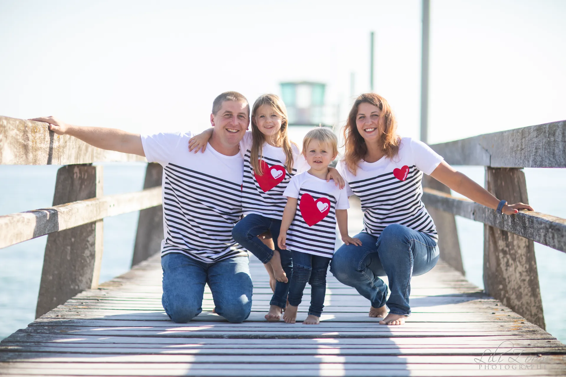 Famille complice en marinières souriant sur un ponton en bois face à la mer - Photographe Famille à Luc-sur-Mer