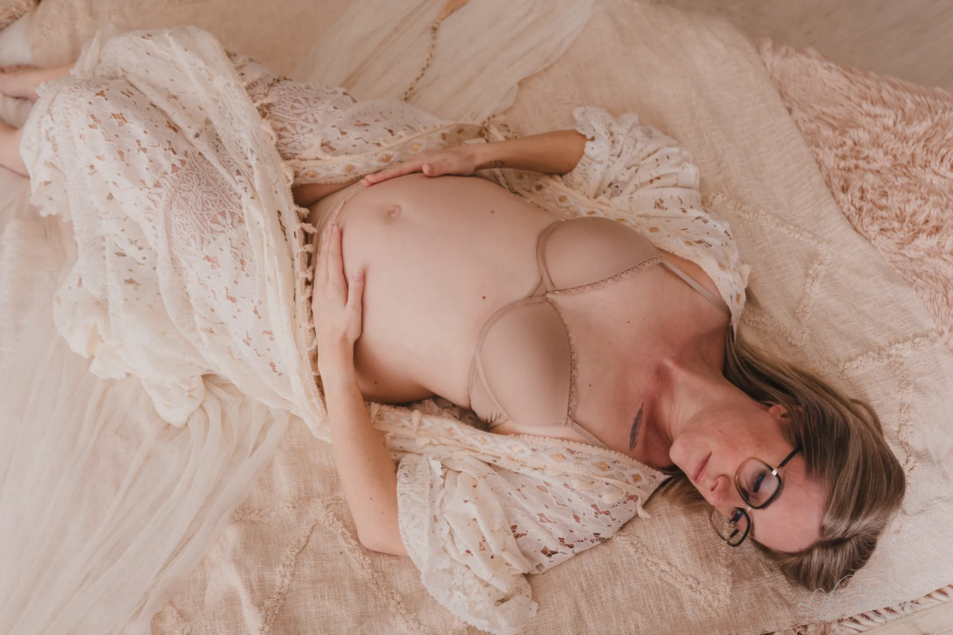Future maman allongée sereinement mettant en valeur son ventre rond dans une robe en dentelle délicate - Photographe Grossesse à Giberville