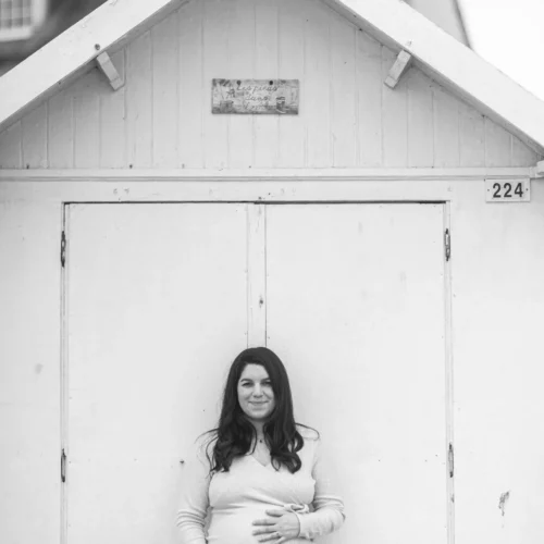 Une femme enceinte se repose sur une cabine de plage de la côté normande, shooting grossesse professionnel en extérieur à Luc sur Mer