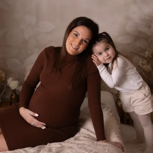 Une femme enceinte et sa petite fille sourient sur un lit dans une chambre bohème, séance grossesse en famille au studio de Giberville