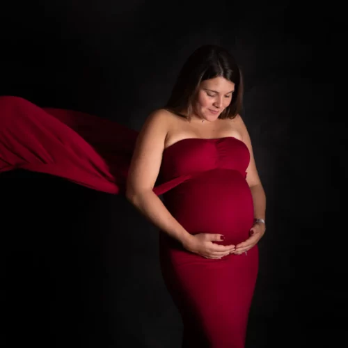 Une future maman en robe rouge tient son ventre rond en studio, séance grossesse à Caen