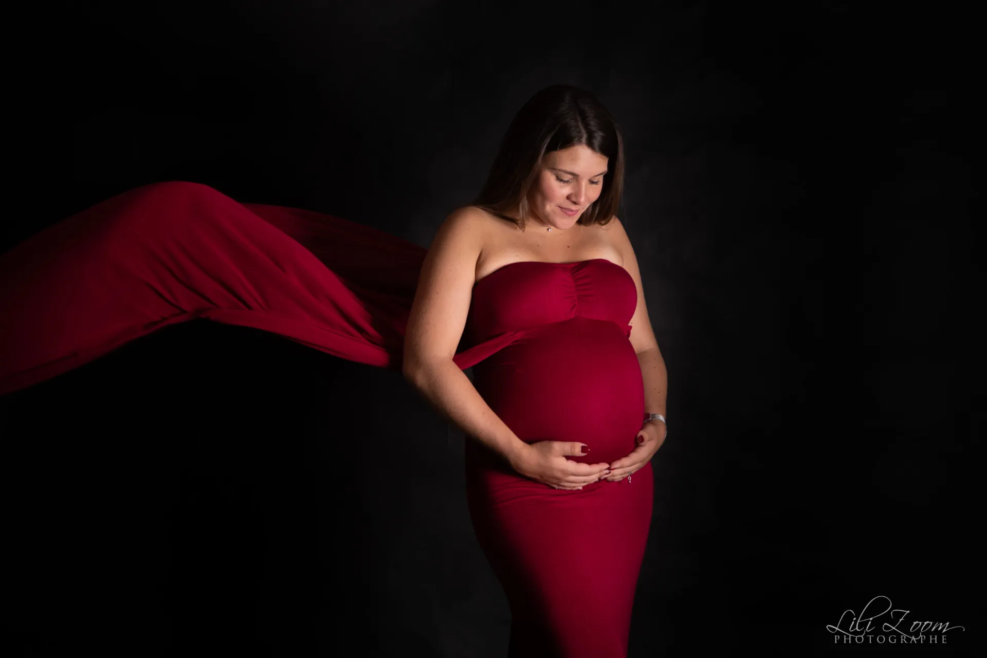 Une future maman en robe rouge tient son ventre rond en studio, séance grossesse à Caen