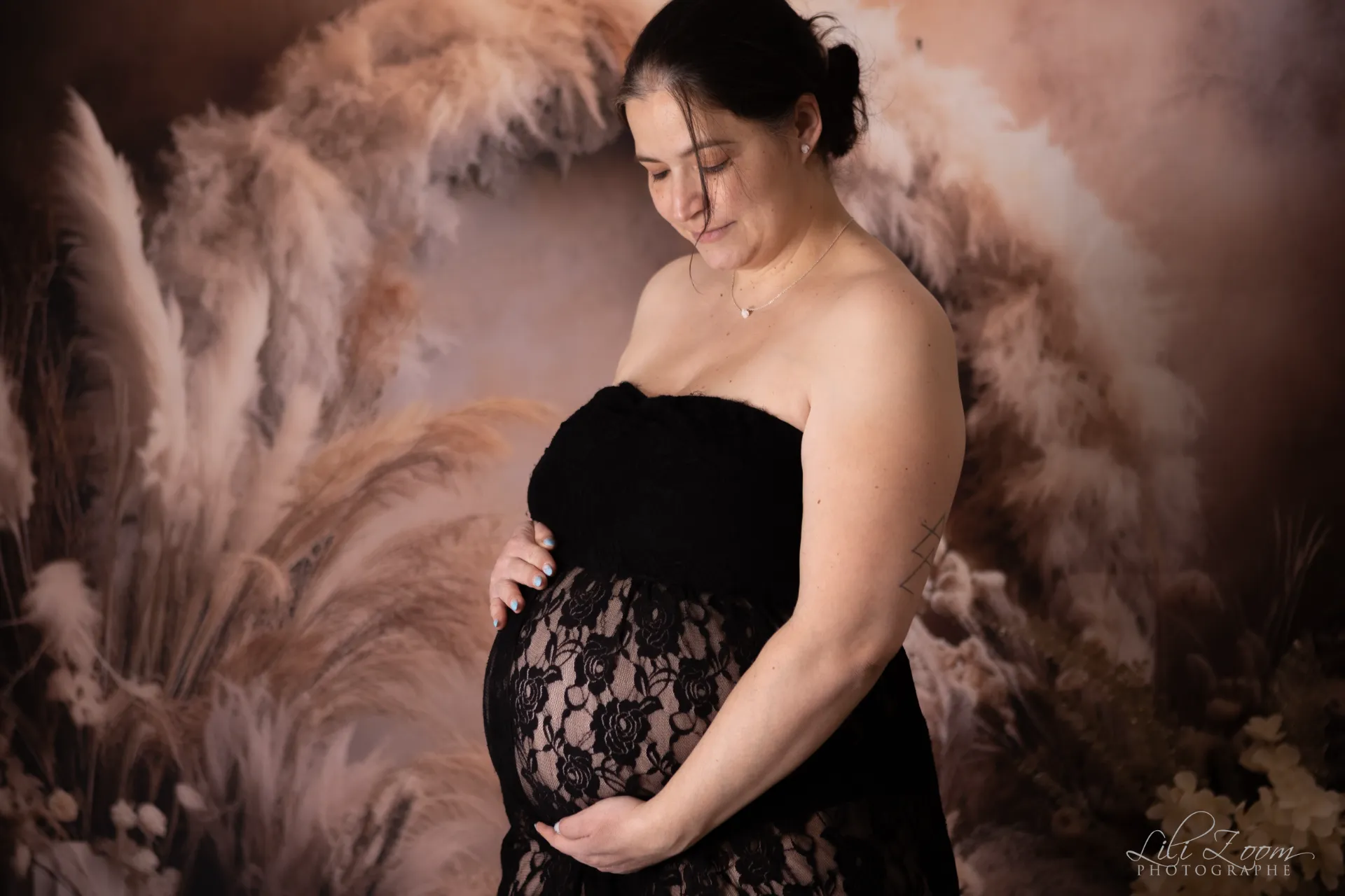 Une femme enceinte porte une tenue fine dans un décor de plumes et de fleurs de pampa, séance photo grossesse en Normandie