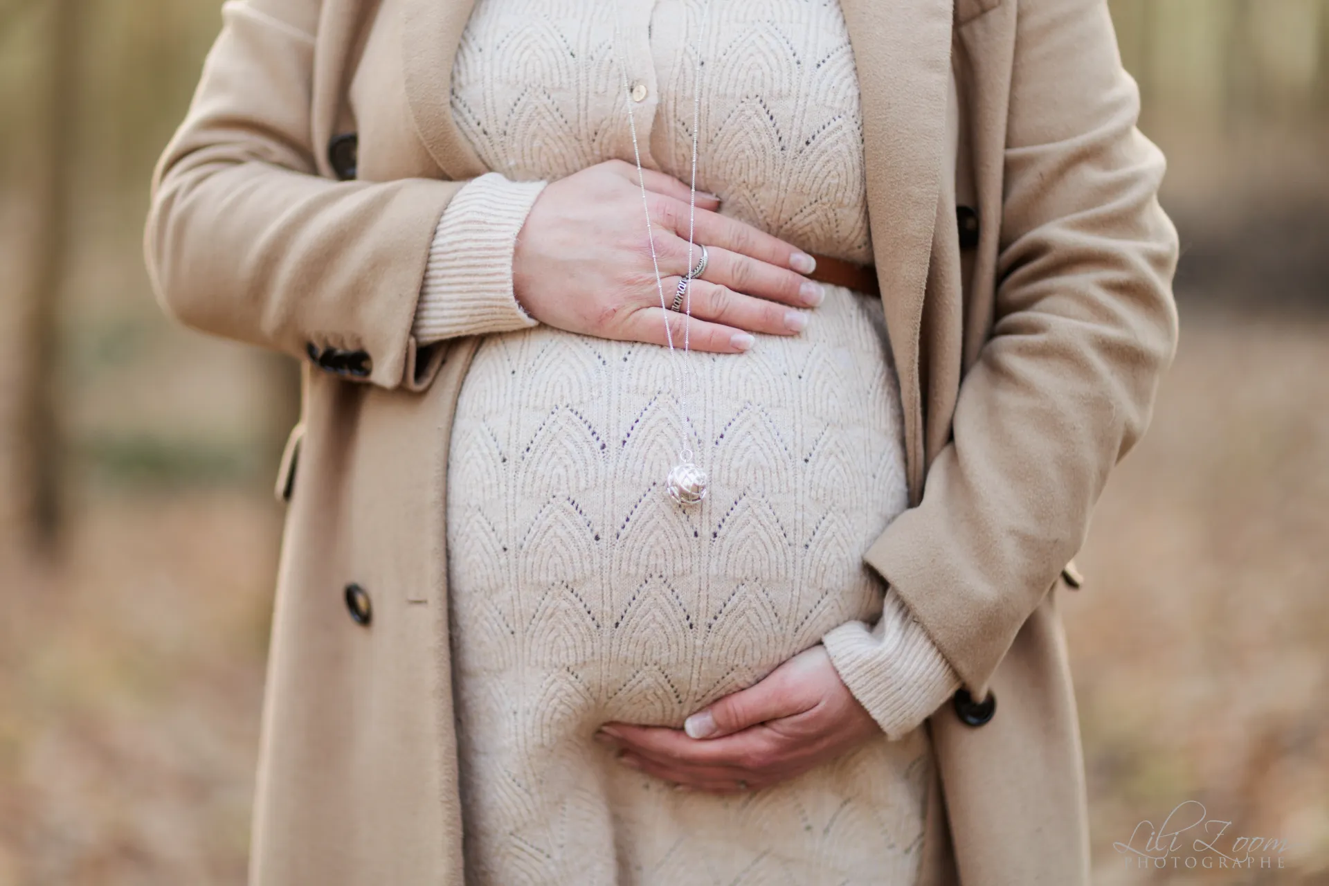 Femme enceinte en manteau de laine tient son ventre dans une forêt d'hiver, séance grossesse à Ifs