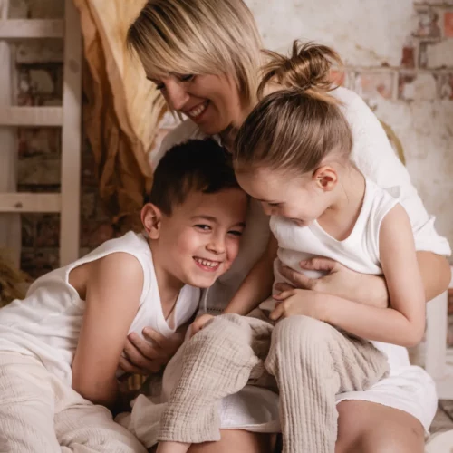 Maman et ses deux enfants partageant un moment de rire et de complicité dans un décor de studio bohème - Photographe Famille secteur Colombelles