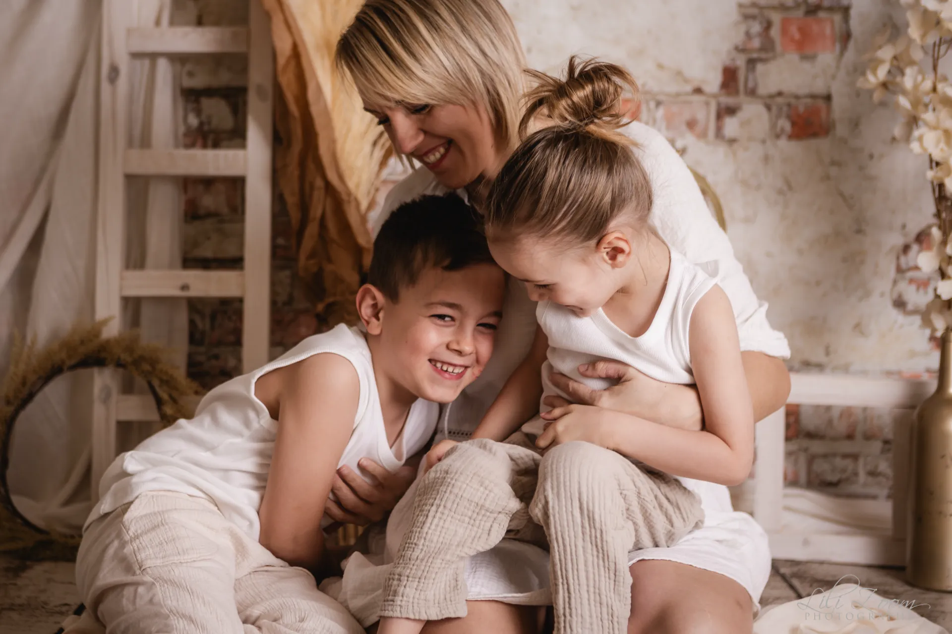 Maman et ses deux enfants partageant un moment de rire et de complicité dans un décor de studio bohème - Photographe Famille secteur Colombelles