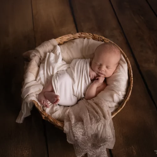 Nouveau-né paisiblement endormi dans un panier d'osier et des voilages délicats sur un parquet en bois - Photographe Naissance proche de Mondeville