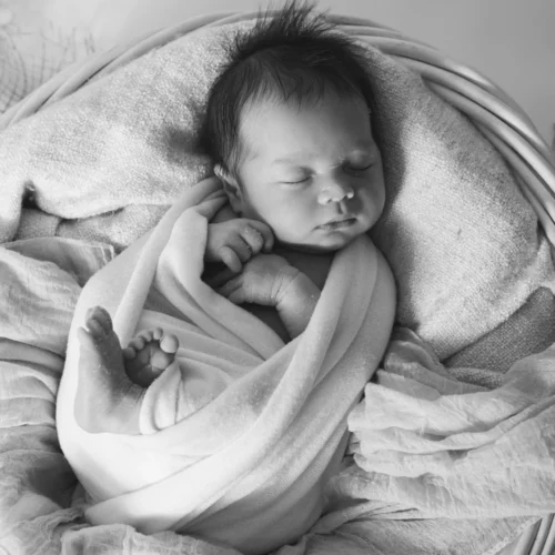 Nouveau-né paisiblement endormi et emmailloté dans un petit panier en osier en noir et blanc - Photographe Naissance aux alentours de Colombelles
