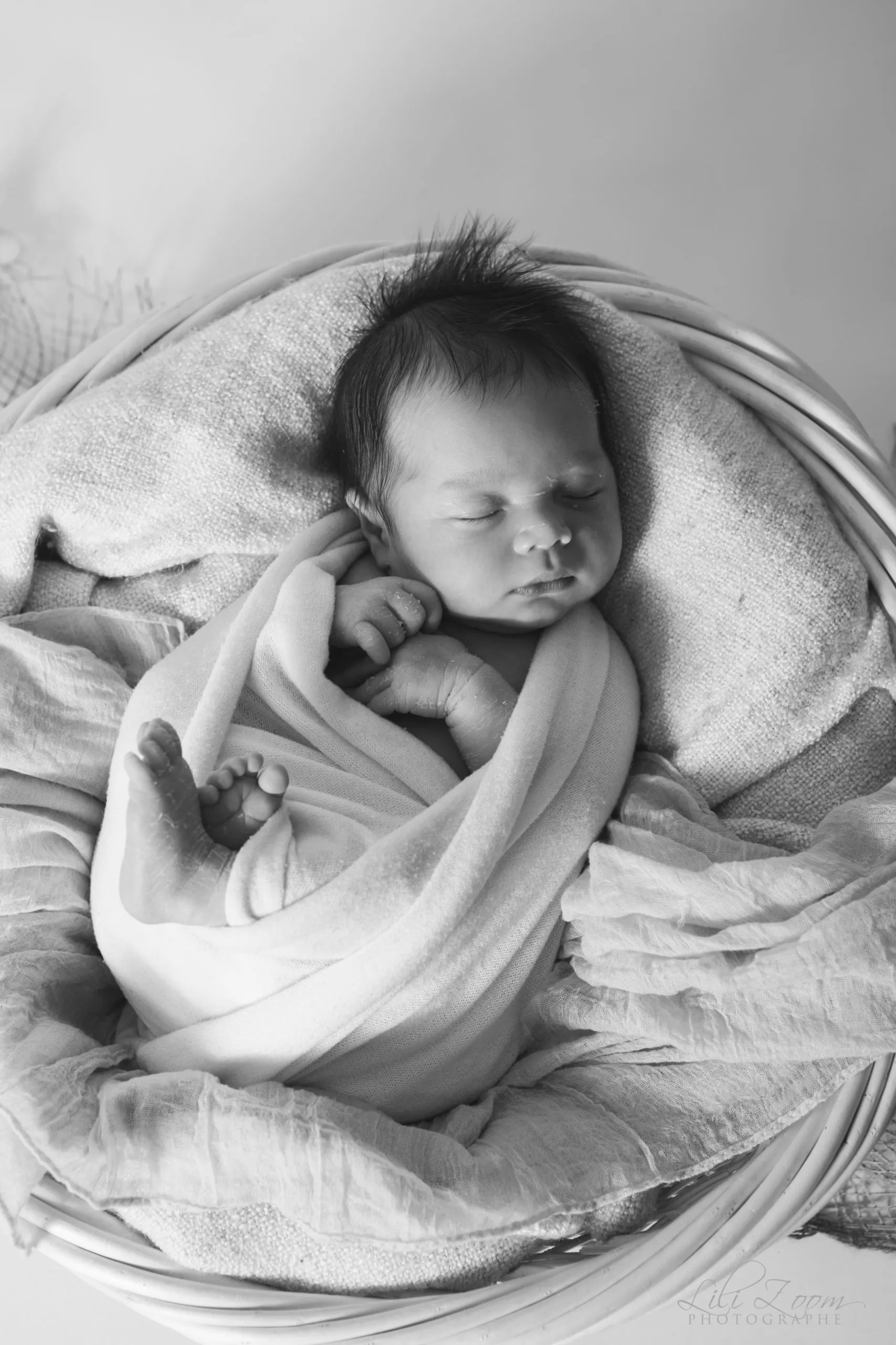 Nouveau-né paisiblement endormi et emmailloté dans un petit panier en osier en noir et blanc - Photographe Naissance aux alentours de Colombelles