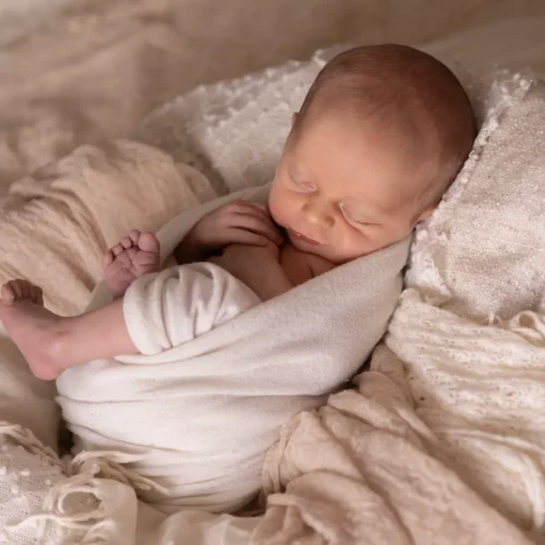 Nouveau-né paisiblement endormi dans un cocon de tissus doux et texturés aux tons crème - Photographe Naissance proche de Colombelles