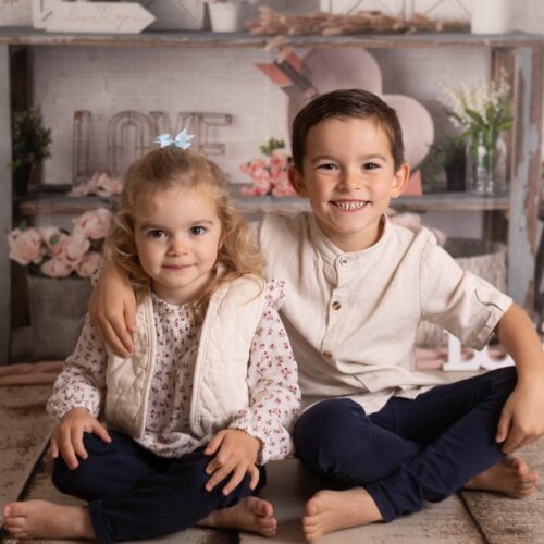 Une soeur et un frère sourient dans un décor bohème aux couleurs naturelles, séance famille entre enfants à Giberville