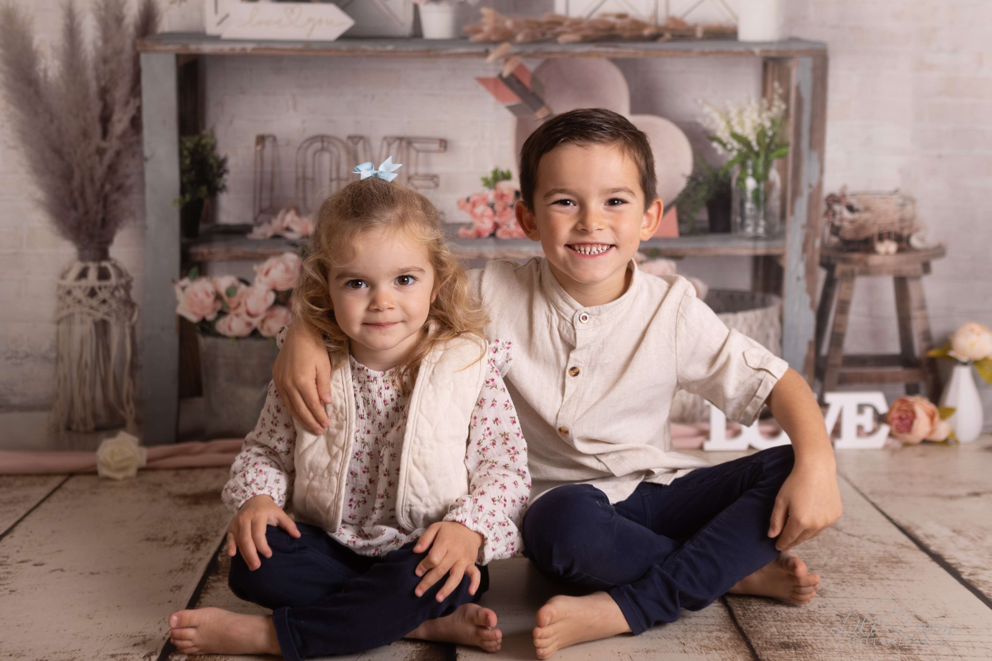 Une soeur et un frère sourient dans un décor bohème aux couleurs naturelles, séance famille entre enfants à Giberville