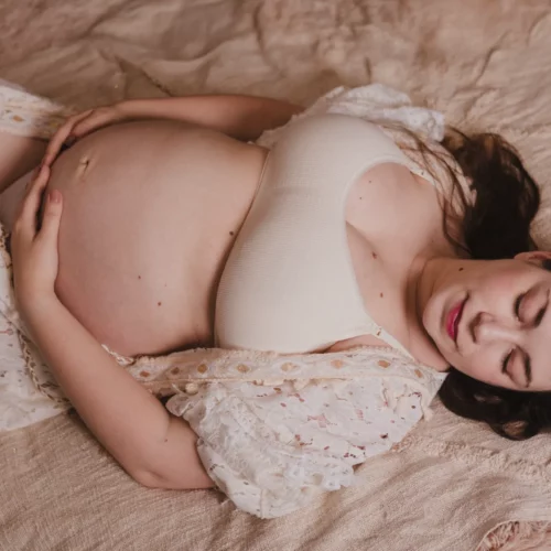 Shooting grossesse d'une femme en robe bohème dans un lit aux couleurs chaudes, séance en studio dans le Calvados
