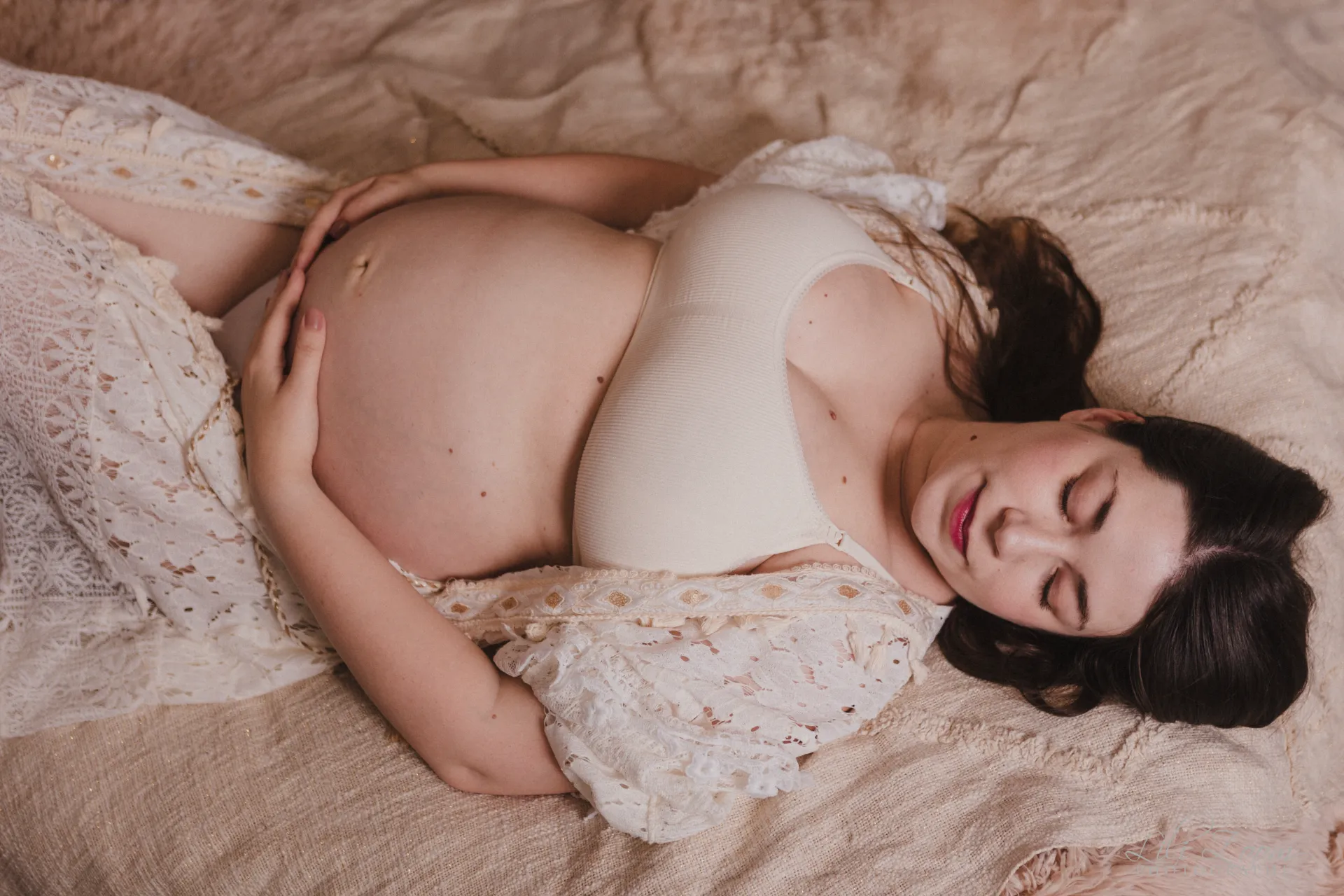 Shooting grossesse d'une femme en robe bohème dans un lit aux couleurs chaudes, séance en studio dans le Calvados