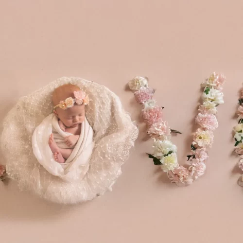 Nouveau-né paisible emmailloté dans un cocon formant le mot LOVE avec des fleurs délicates - Photographe Naissance à Giberville