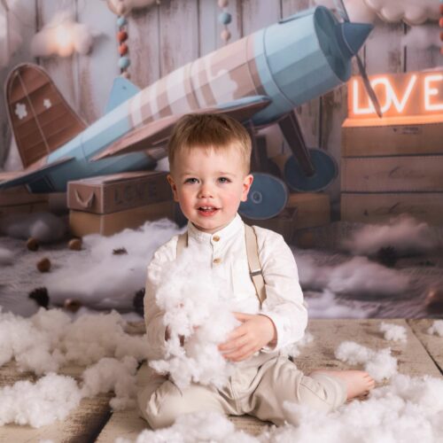 Un petit garçon avec des bretelles dans un décor d'avion dans les nuages et les lettres LOVE, séance photo féérique dans le Calvados