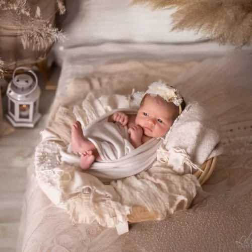 Nouveau-né paisible avec un bandeau fleuri, emmailloté dans un décor de studio bohème aux tons naturels - Photographe Naissance proche de Hérouville-Saint-Clair