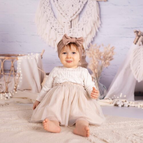 Une petite fille porte un bandeau rose à dentelles sur un tapis bohème avec un tipi blanc, shooting photo bébé dans le Calvados