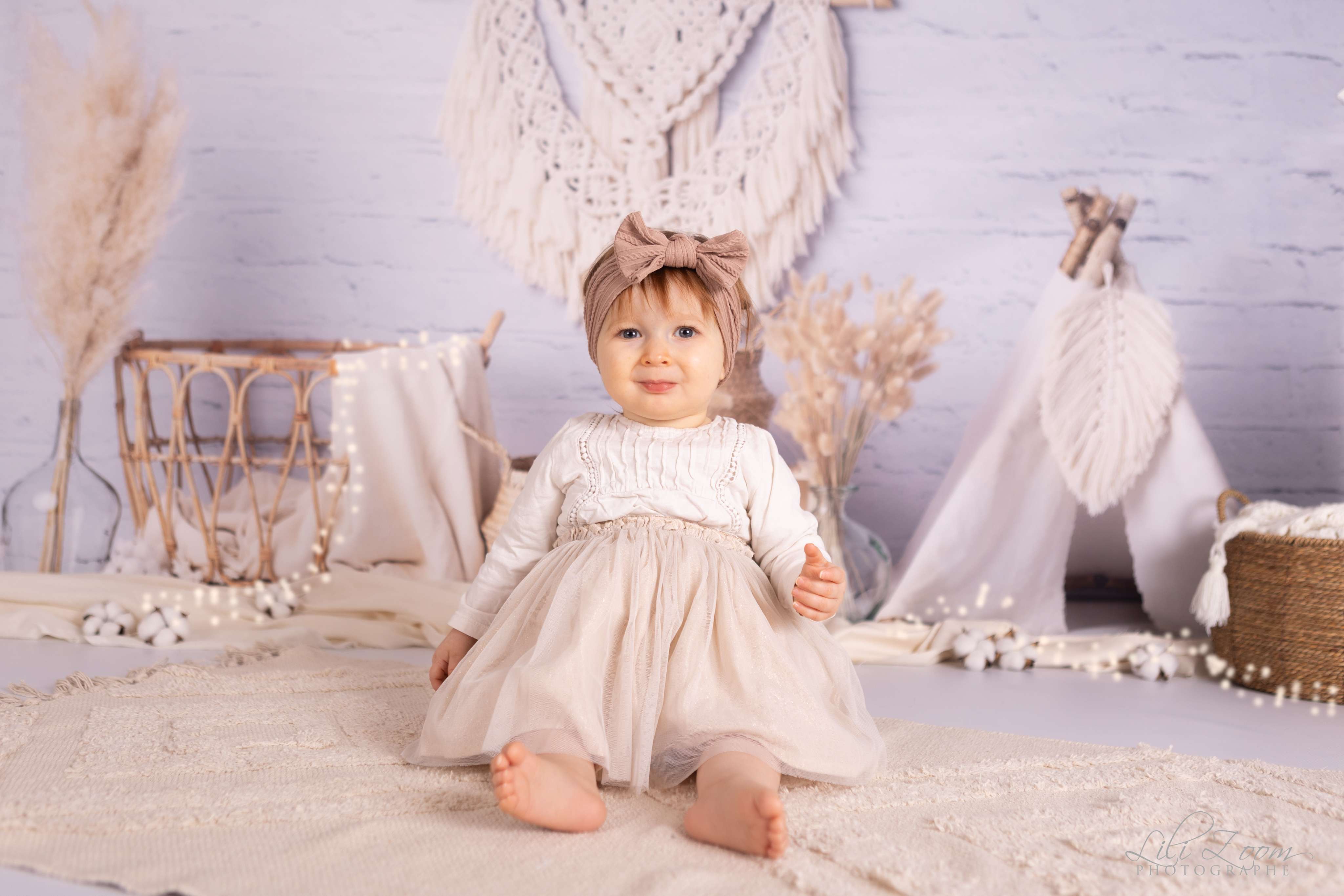Une petite fille porte un bandeau rose à dentelles sur un tapis bohème avec un tipi blanc, shooting photo bébé dans le Calvados