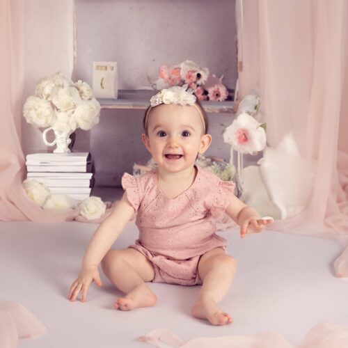 Un bébé habillé en rose avec un ruban sur le thème du printemps avec des fleurs et des voilures roses, séance photo douceur et romantique à Caen