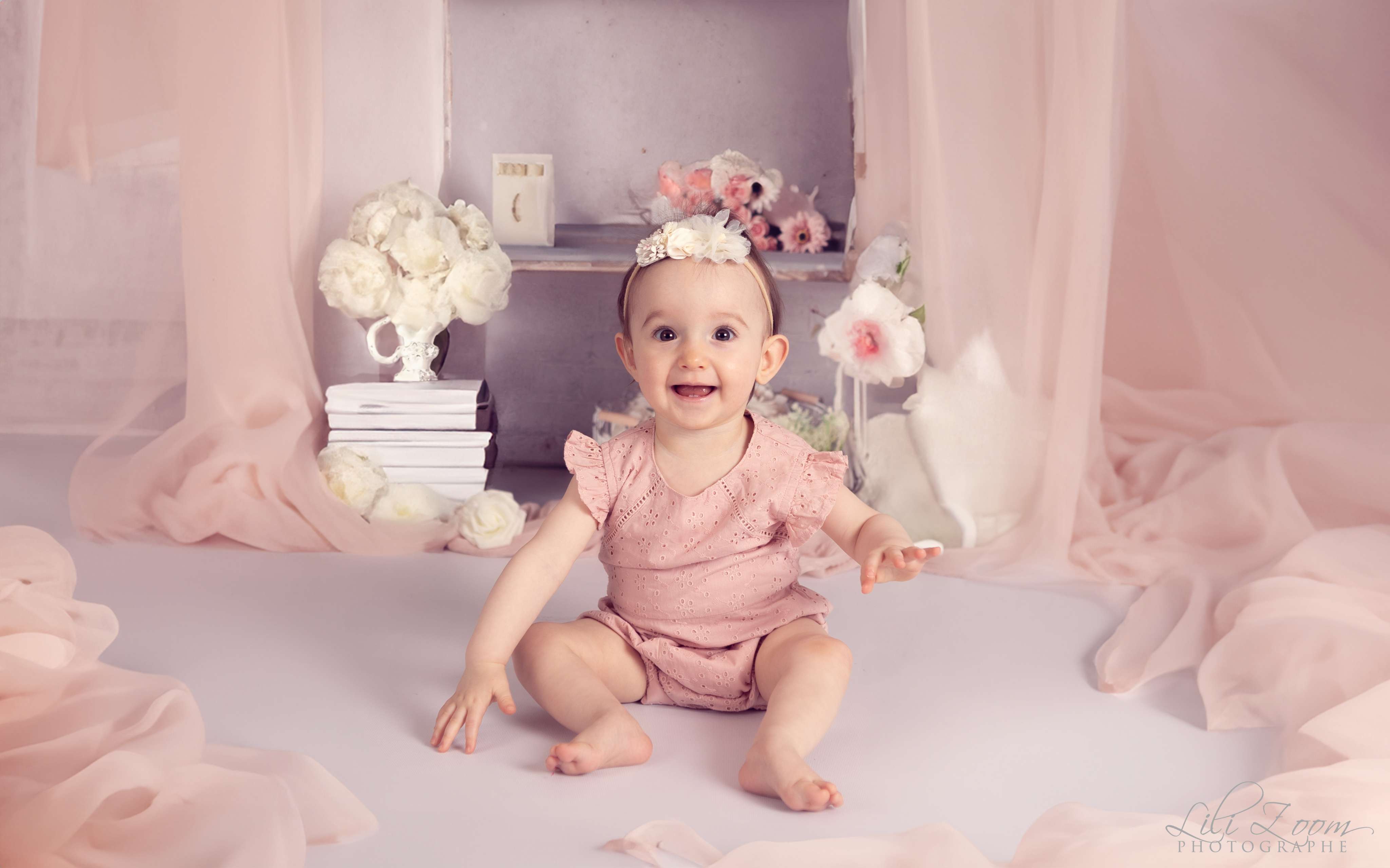 Un bébé habillé en rose avec un ruban sur le thème du printemps avec des fleurs et des voilures roses, séance photo douceur et romantique à Caen