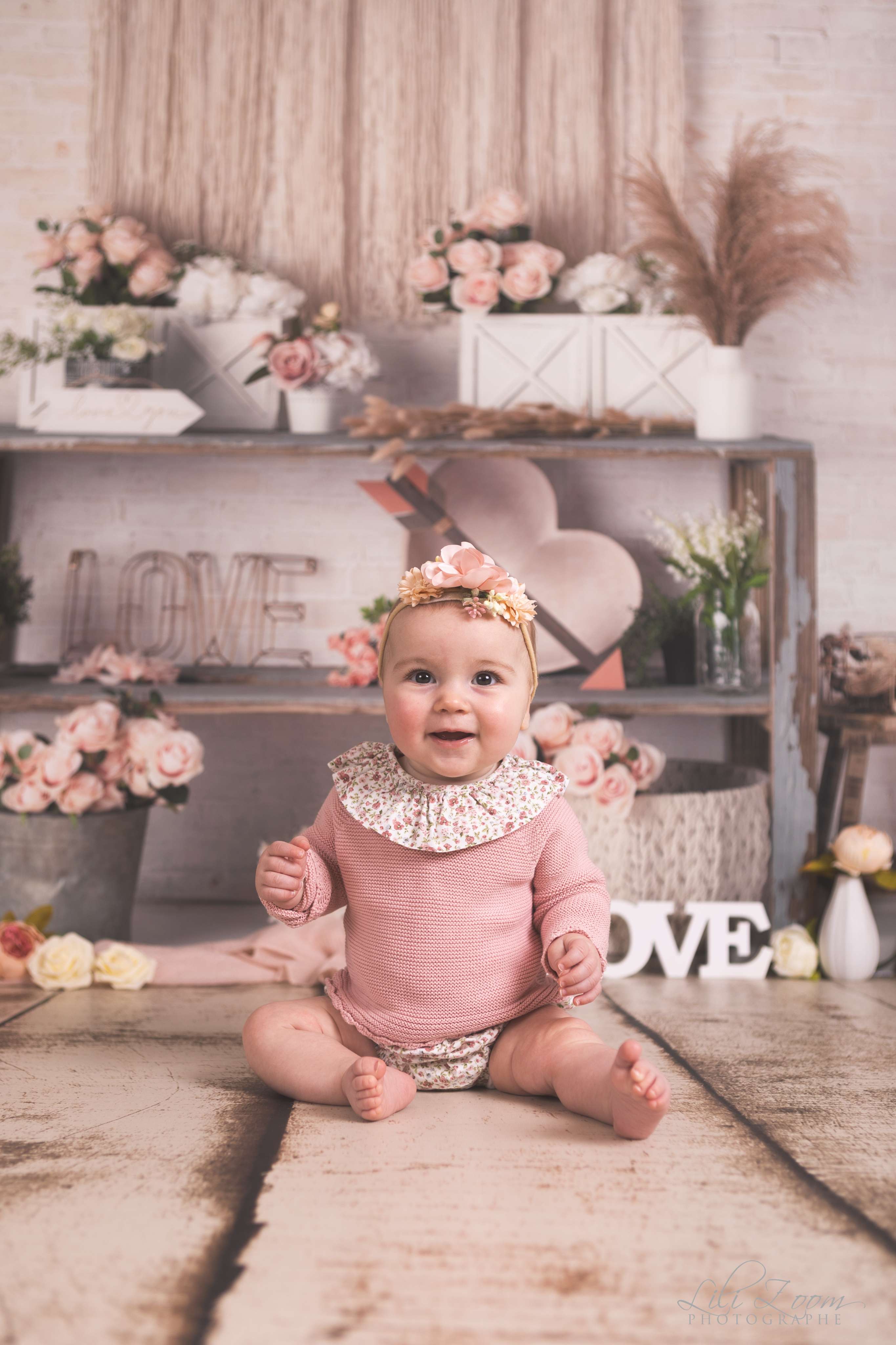 Un bébé avec un ruban de fleurs sur la tête, dans une petite tenue rose pose dans un décor bohème romantique, séance photo bébé à Caen