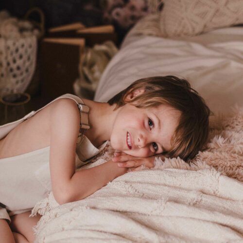 Une enfant au regard doux est posée sur un lit en dentelles, séance nature en studio en Normandie