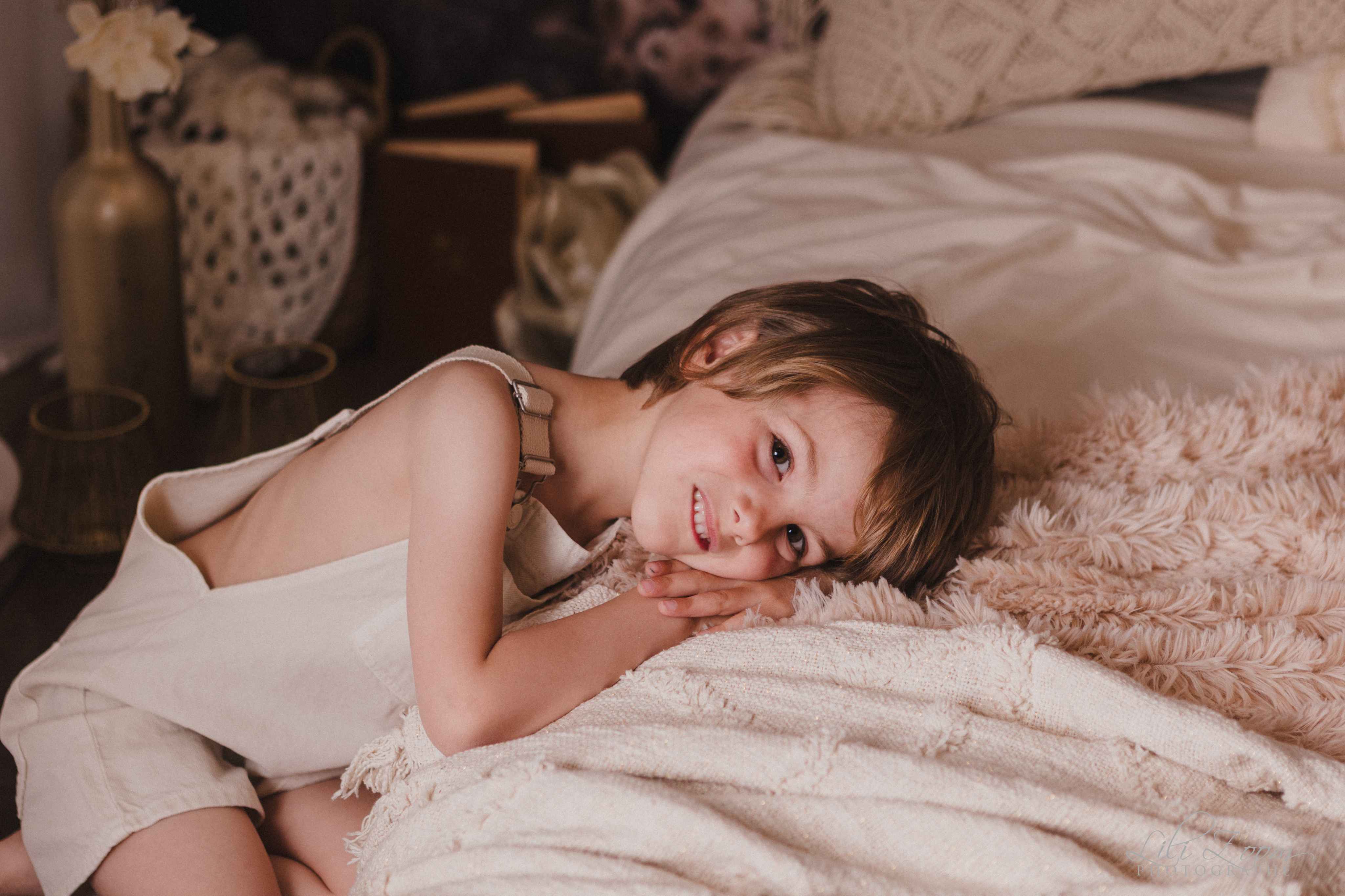 Une enfant au regard doux est posée sur un lit en dentelles, séance nature en studio en Normandie