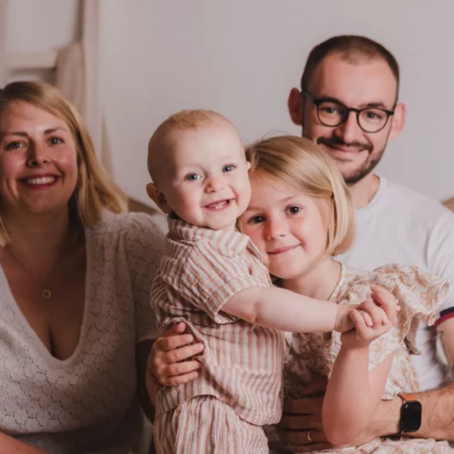 Portrait rayonnant d’une famille complice et ses deux jeunes enfants dans un décor de studio doux et bohème - Photographe Famille à Giberville