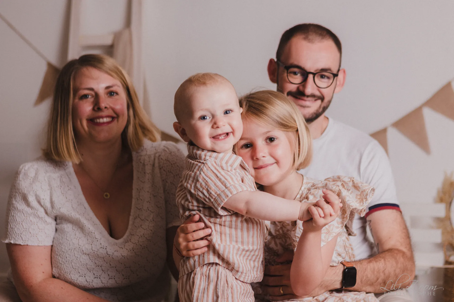 Portrait rayonnant d’une famille complice et ses deux jeunes enfants dans un décor de studio doux et bohème - Photographe Famille à Giberville