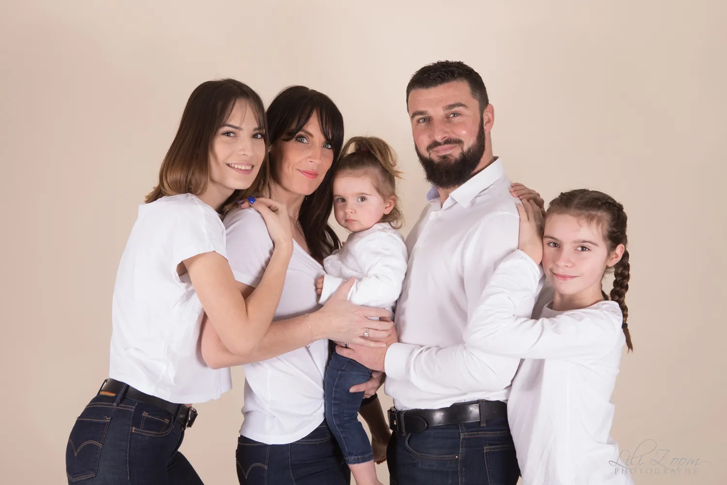 Une famille nombreuse s'enlace sur un fond couleur nature en studio photographique, photographe de portrait de famille en Normandie