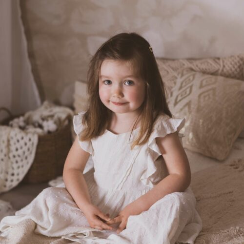 Une petite fille en robe blanche dans une chambre à la décoration naturelle et douce, séance enfant à Mondeville