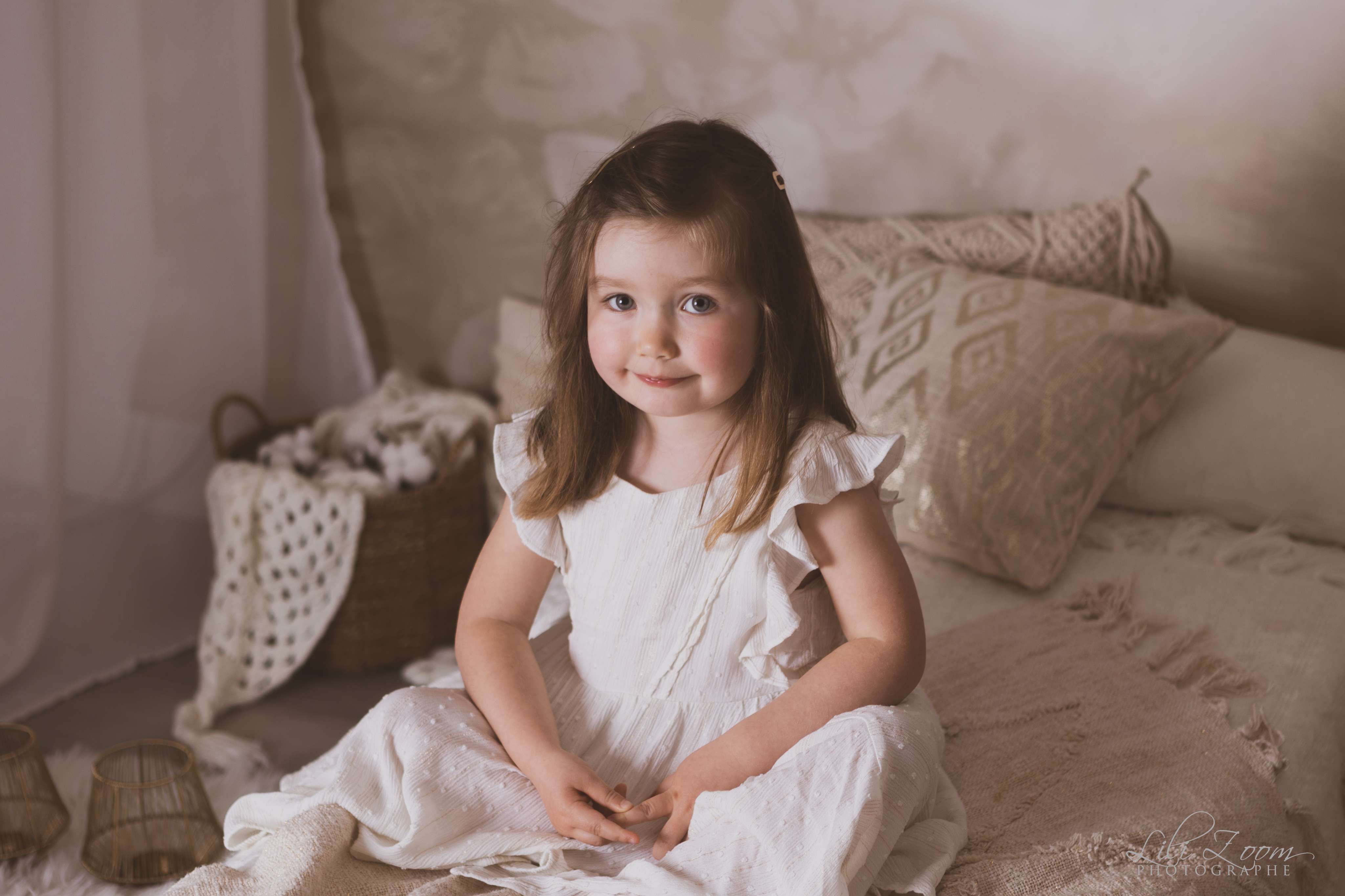 Une petite fille en robe blanche dans une chambre à la décoration naturelle et douce, séance enfant à Mondeville