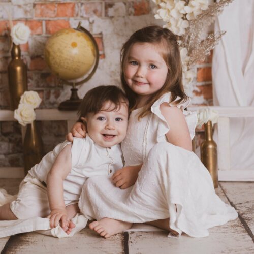 Une soeur et son frère posent devant une mappemonde et un mur de briques, séance photo fratrie à Ifs