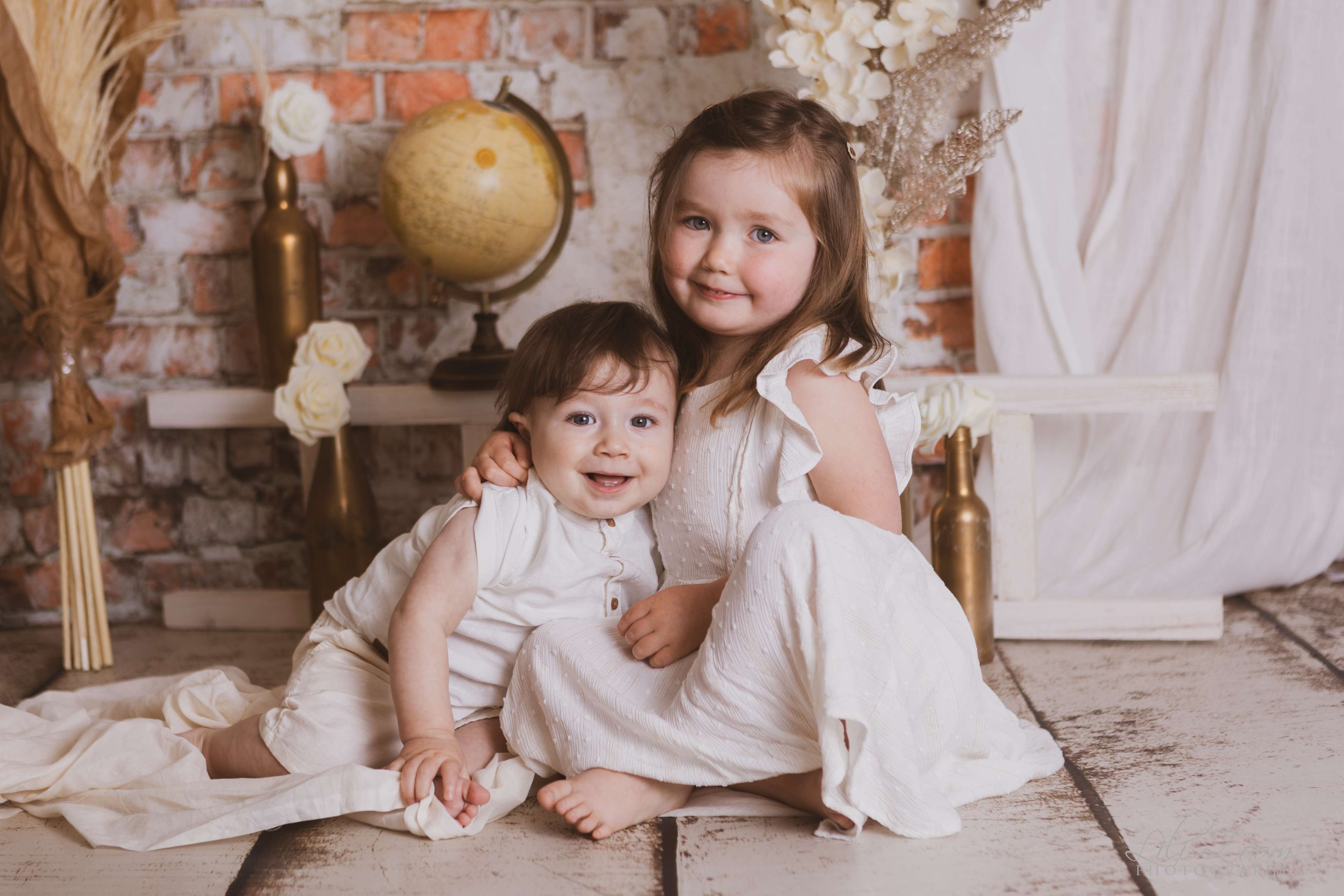 Une soeur et son frère posent devant une mappemonde et un mur de briques, séance photo fratrie à Ifs