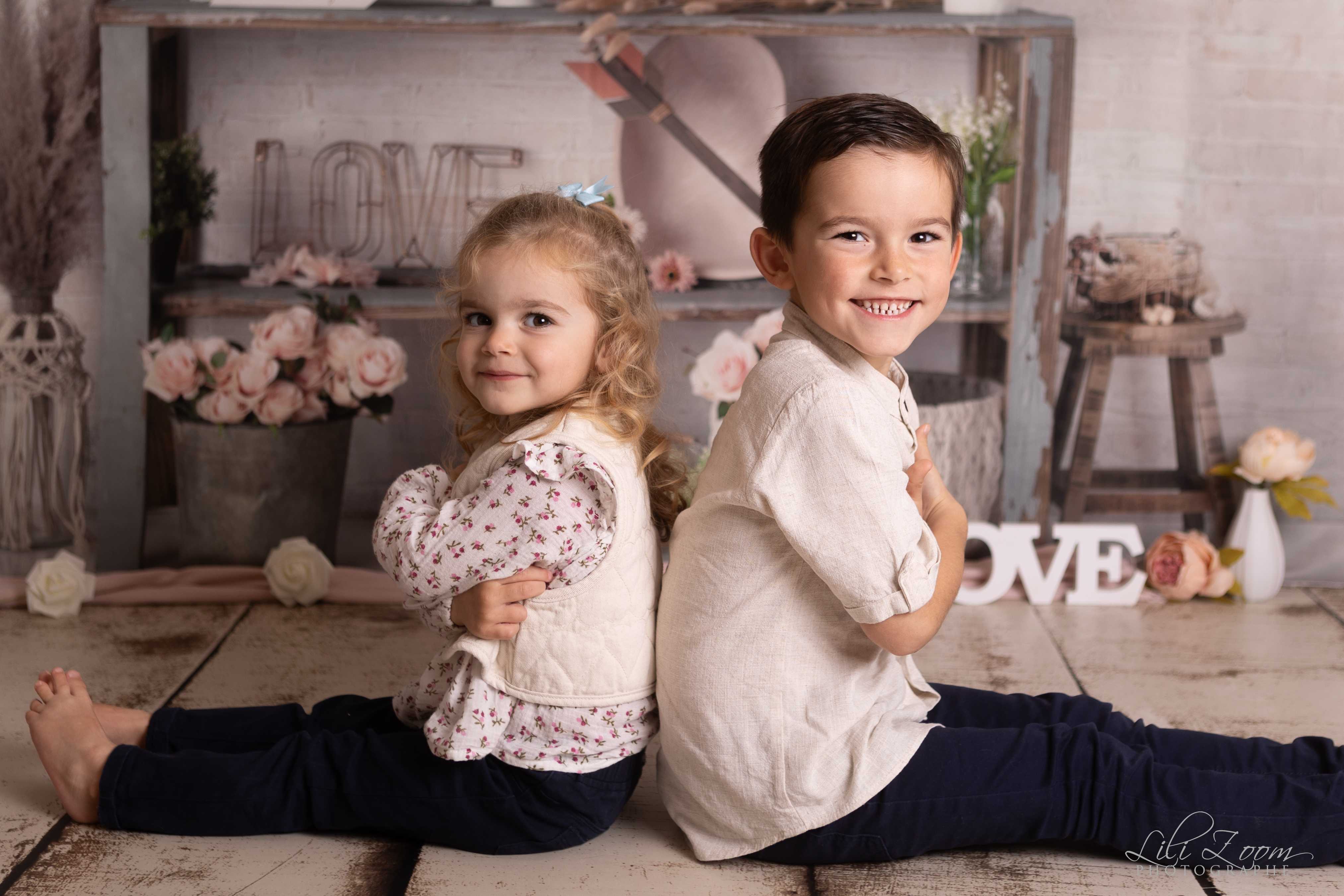 Une soeur et un frère sont dos à dos et sourient pendant une séance photographique en famille à Giberville