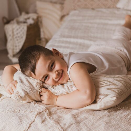 Un enfant posent allongé sur un lit, les couleurs sont douces et naturelles, ambiance bohème pendant un shooting photo en Normandie