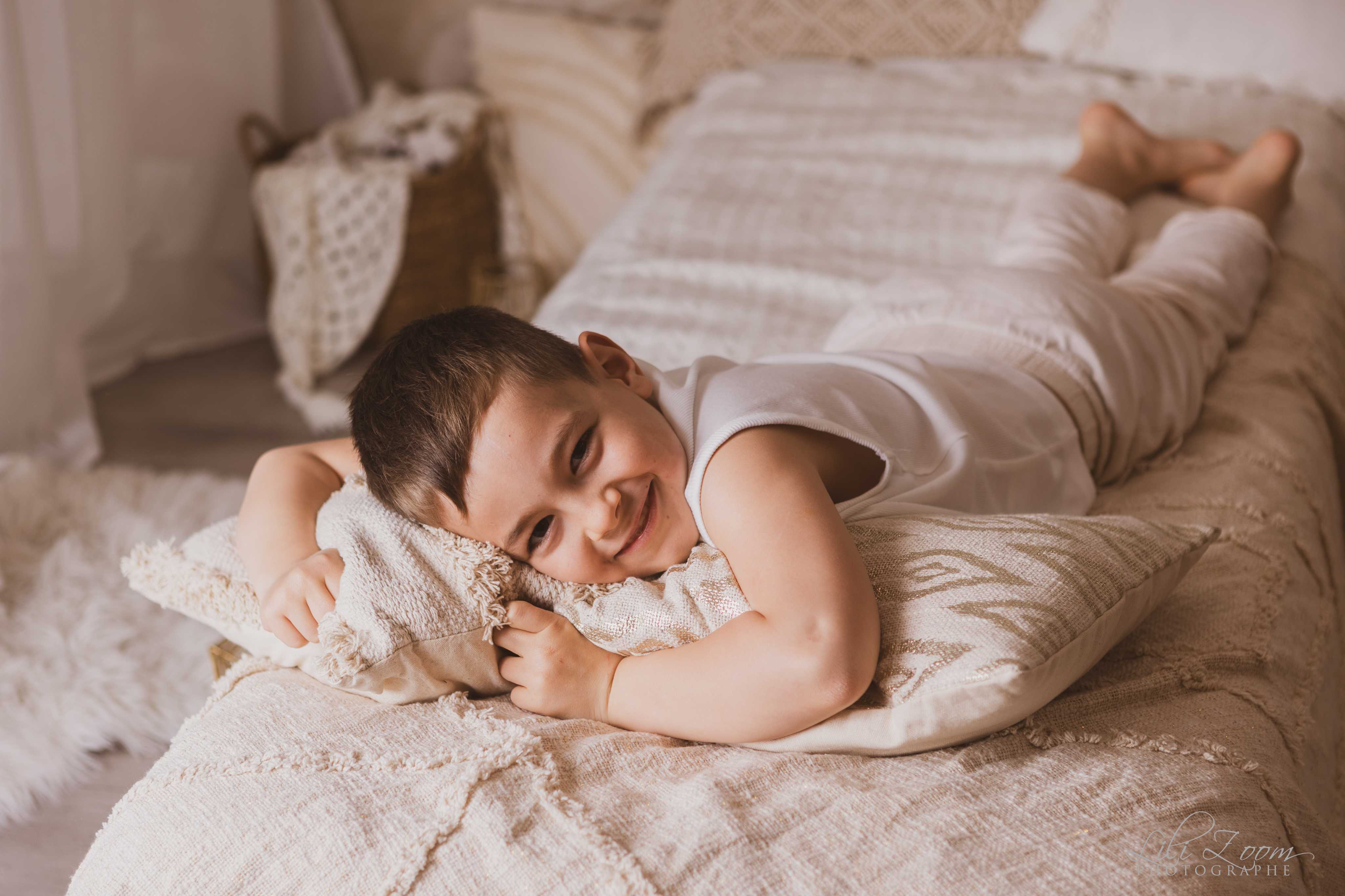 Un enfant posent allongé sur un lit, les couleurs sont douces et naturelles, ambiance bohème pendant un shooting photo en Normandie