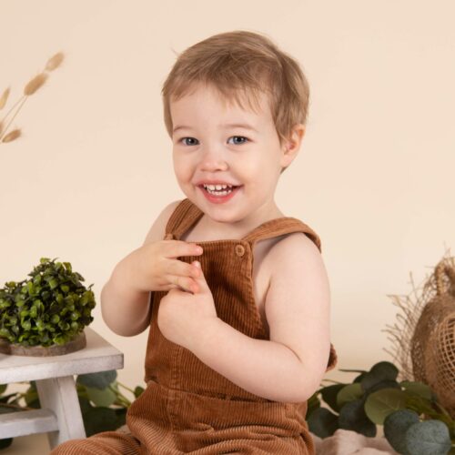 Un enfant en salopette sourie dans un décor champêtre et naturel avec de la paille et des brins de blé, séance photo décorée à Caen