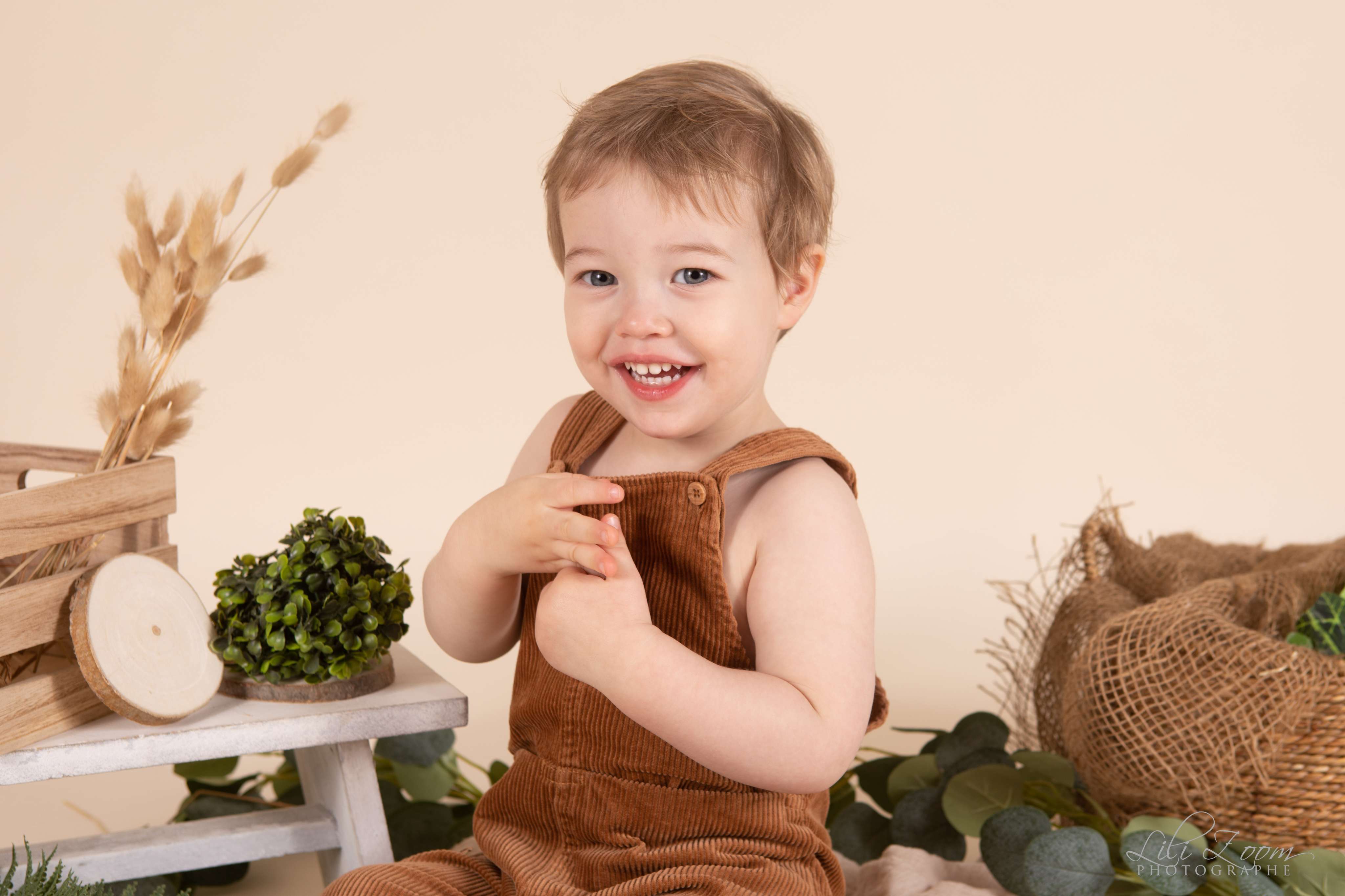 Un enfant en salopette sourie dans un décor champêtre et naturel avec de la paille et des brins de blé, séance photo décorée à Caen